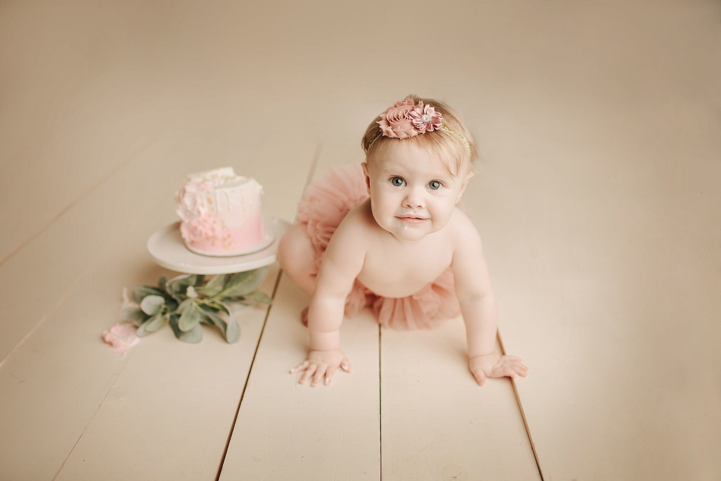Baby sitting beside a messy cake during cake smash session.